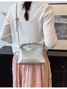 Chic silver crossbody bag with metal chain strap and ball charm shown on a model