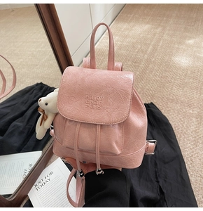 Detail of pink crinkled PU leather mini backpack with embossed text and bear charm
