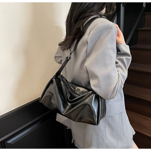 Detailansicht der schwarzen glänzenden Schultertasche mit grauem Blazer am Modell
