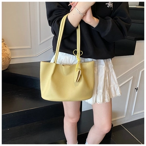 Detail of yellow litchi pattern tote bag with heart charm shown on a shoulder strap