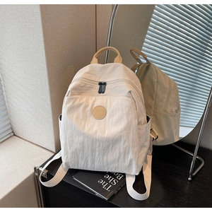 Detail of cream nylon backpack with front pocket and round logo patch shown in mirror
