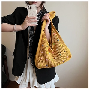 Detail of yellow knit tote bag with colorful faux pearl beads on a black blazer backdrop