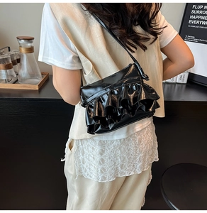 Close-up of black ruffled pleated shoulder bag in glossy patent leather on model