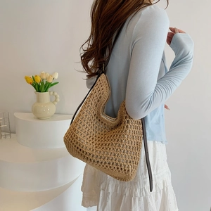 Detail of handwoven hobo bag in beige straw texture with slim brown leather shoulder strap