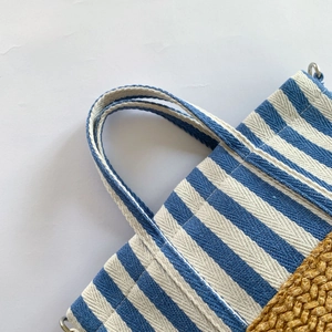 Detail of blue striped canvas tote with woven straw base and metal strap hardware