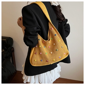 Detail of yellow knit hobo bag with colorful pearls on a black blazer backdrop