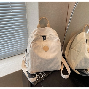 Detail view of a cream white nylon backpack with a brown leather logo and top handle