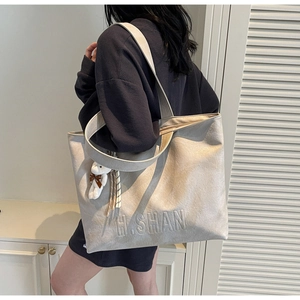 Detail of cream tote bag featuring embossed H.SHAN lettering and cute bear charm pendant