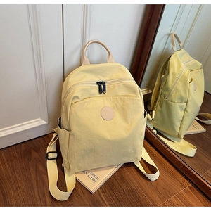 Detail of light yellow canvas backpack with leather handle and side pockets on a book