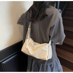 Detail einer weißen Lackleder-Schultertasche mit natürlicher Faltenstruktur an einem Modell