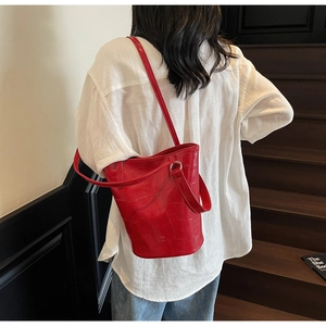 Detail of red croc-embossed bucket bag worn by model on a wooden staircase