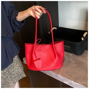 Detail of red litchi texture leather tote bag with stylish pendant in a home setting