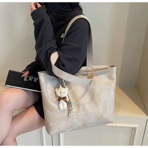 Detail of beige tote bag featuring vintage pleated texture and plush bear charm