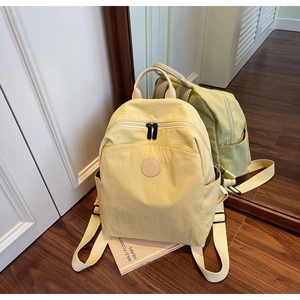Detail view of a beige lightweight nylon backpack with a round leather logo on wood floor