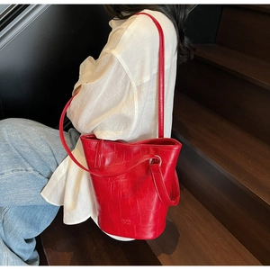 Detail view of red crocodile pattern bucket bag with brand logo and slender shoulder strap