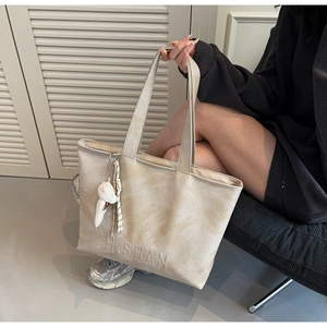 Detail of cream leather tote bag with embossed logo and decorative bear charm