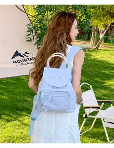 Outdoor view of a light blue nylon backpack featuring rainbow letters and rope handle
