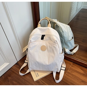 Detailed close-up of a beige lifestyle backpack with leather logo and textile texture