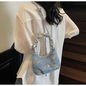 Detailed shot of a blue denim dumpling bag with silver butterfly and chain strap