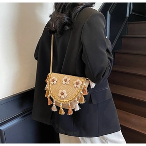 Detail of woven straw crossbody bag with floral accents and soft tassel fringe trim