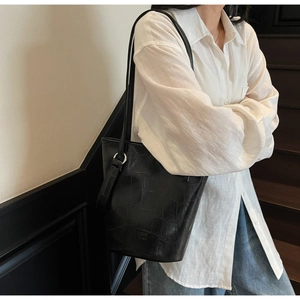 Detailed view of black crocodile pattern leather bucket bag with silver hardware on model