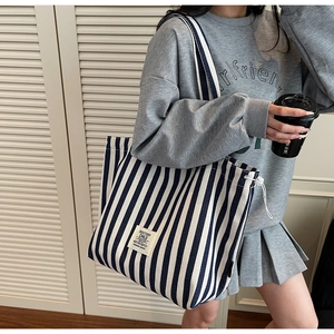 Detail of canvas tote bag showing blue vertical stripes and side drawstring adjustment