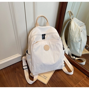 Detail view of cream backpack with brown leather handle and circular logo on wooden floor