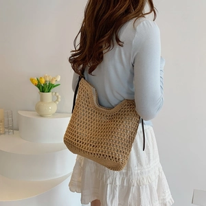 Detail of hand-woven straw hobo bag with brown leather strap and hollow mesh pattern