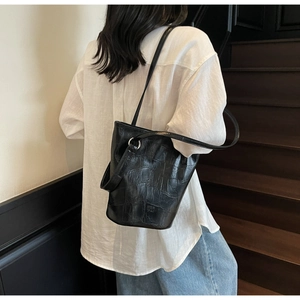 Detail of black crocodile texture bucket bag with MER PAI logo on white shirt backdrop