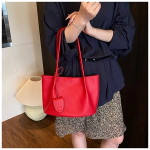 Detail of red lychee grain leather tote bag with circular pendant in a lifestyle setting