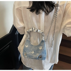 Dettaglio borsa a tracolla in denim blu con patch a farfalla specchiate argento e catena
