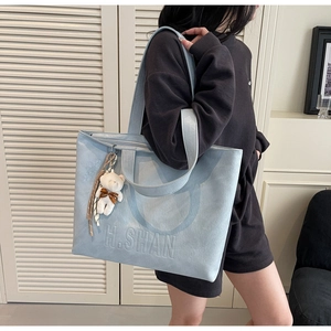 Macro detail of light blue tote bag with embossed H.SHAN logo and cute teddy bear pendant