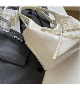 Dettaglio borsa tote in pelle bianco avorio con fiocco di pizzo su sfondo abito grigio