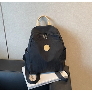 Close-up of black nylon backpack with circular logo badge and beige top handle detail