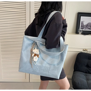 Close-up of light blue tote bag with embossed H.SHAN text and cute plush bear charm