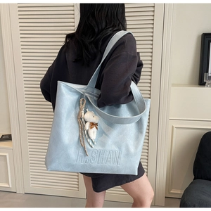 Detail view of light blue leather tote bag with brand logo and plush bear charm