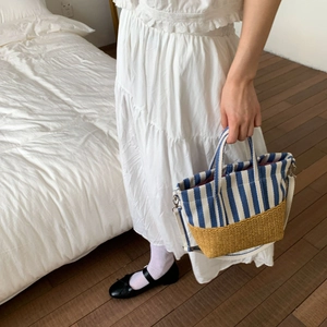 Detail of canvas striped and straw woven tote bag held by a model in a white dress
