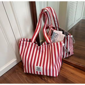 Detail of red and white striped canvas tote bag with drawstring closure on wooden floor