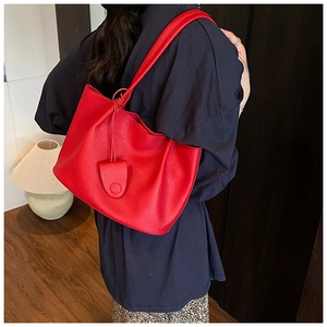 Close-up of red pebbled leather tote bag with knotted shoulder strap and stylish charm