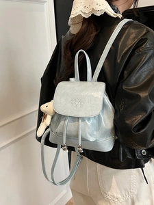 Ice blue bucket backpack in wrinkled faux leather featuring a plush bear charm on model