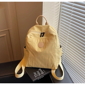 Close-up of light yellow nylon backpack showing dual zippers and round leather patch