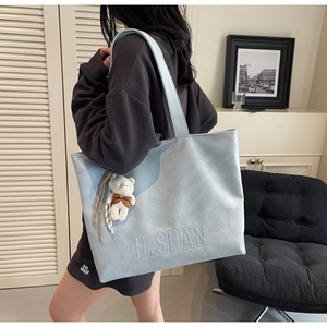 Detail of light blue tote bag with embossed H.SHAN logo and white plush bear charm