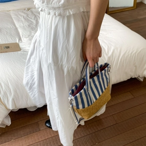 Detail of canvas striped tote with woven straw base and wine-red lining on a bed