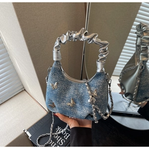 Detailed macro view of light blue denim crescent bag with metallic butterfly accents
