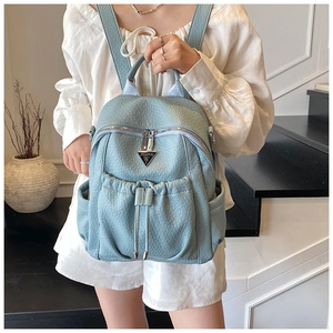 Detail of light blue textured leather backpack with silver zippers and metal logo plate