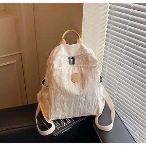 Detail of cream nylon backpack with leather handle and round logo on a black stool