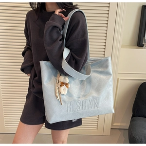 Detail of light blue textured leather tote bag with H.SHAN embossed logo and bear charm