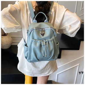 Detail of light blue backpack with drawstring pocket and metallic triangular logo plate