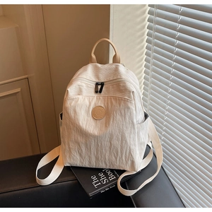 Close-up of off-white nylon backpack with round logo and leather handle on a book