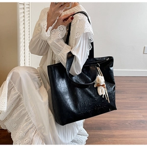 Detail of black textured leather tote bag with MARSH embossing and white teddy bear charm